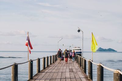 People on pier over sea against sky