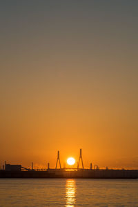 Silhouette bridge over sea against sky during sunrise