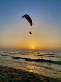 Silhouette person paragliding at beach against sky during sunset