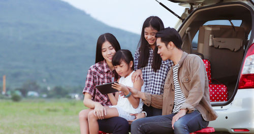 Friends spending leisure time against car on field 