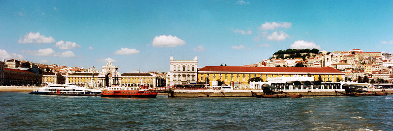 Boats in harbor by river against blue sky