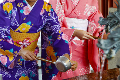 Midsection of women in kimono washing hands at fountain