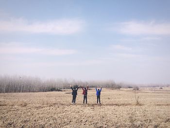 Rear view of men standing on field with arms raised against sky