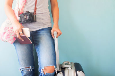 Midsection of woman with luggage standing against wall