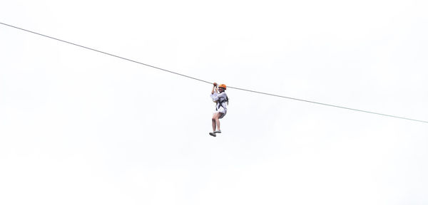Low angle view of man hanging on rope against clear sky