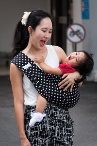 Happy woman carrying baby while standing at city