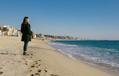 Middle-aged woman standing on the beach looking at the sea on a sunny winter day