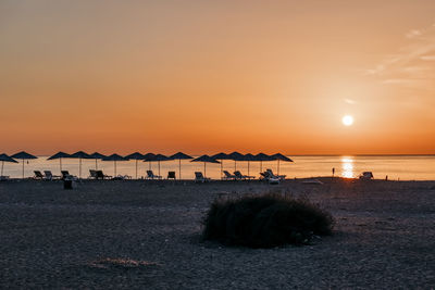 Thatched roofs and lounge chairs on beach during sunset