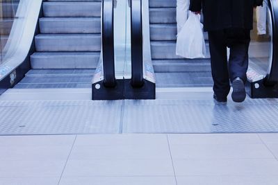 Low section of man with shopping bag on escalator at mall