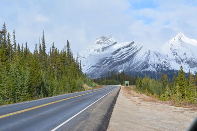 Empty road leading towards snowcapped mountains against cloudy sky