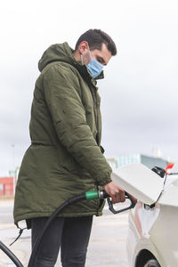 Man with protective face mask refueling car at gas station during covid-19