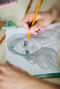 Cropped hands of woman sketching female on paper at table