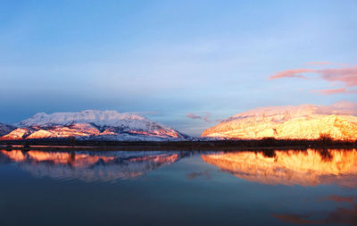 Scenic view of lake by snowcapped mountains against sky during sunset