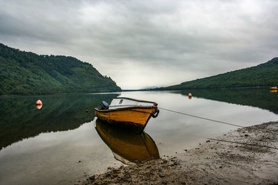 Boats in calm lake against cloudy sky