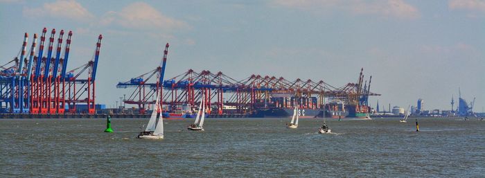 Cranes at pier by sea against sky