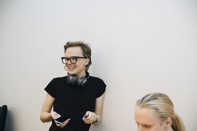 Smiling genderblend business professional looking away while leaning on white wall in illuminated board room