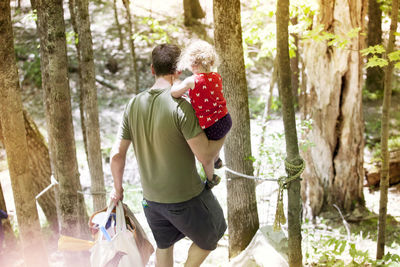 High angle view of father carrying daughter and bags while walking in forest