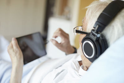 Over the shoulder view of senior man wearing headphones while using digital tablet in hospital