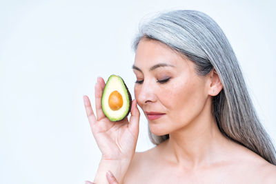 Portrait of young woman holding apple against white background