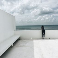 Rear view of woman looking at sea while standing on observation point against cloudy sky