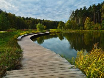 Boardwalk amidst trees by lake against sky