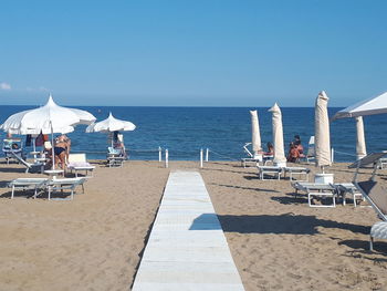 Chairs on beach by sea against blue sky