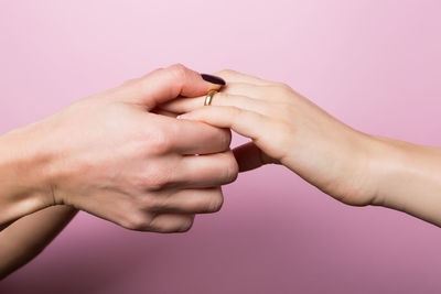 Cropped hand of woman holding friend ring against wall