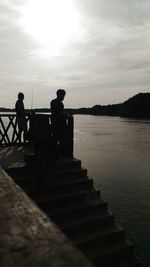 Silhouette people standing on railing by sea against sky