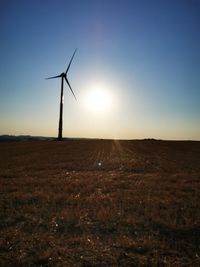 Wind turbines on field against clear sky during sunset