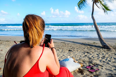 Rear view of woman photographing on beach