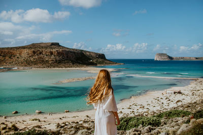 Rear view of woman standing at beach against sky