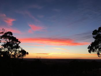 Silhouette trees on landscape against sky at sunset