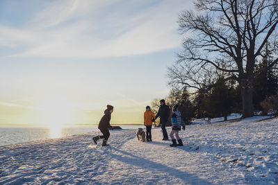 Father and sons walking a dog along a snowy path at sunset.