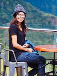 Portrait of smiling young woman sitting at table by railing