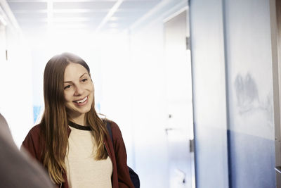 Smiling student looking away while standing in corridor at university
