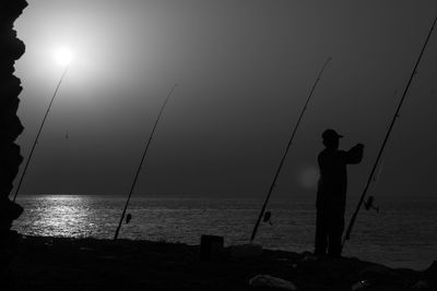 Silhouette man fishing by sea against clear sky