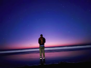 Rear view of man standing at beach against sky at night