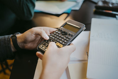 Hands of young male student using calculator at university