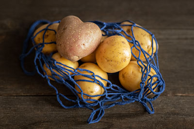 Heart-shaped red potatoes with white potatoes in a blue eco-grid on a wooden background close-up.