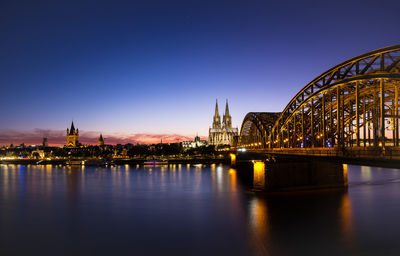 Illuminated bridge over river against sky in city