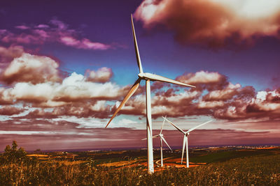 Wind turbines on field against cloudy sky