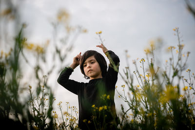 Low angle view on standing girl between yellow flowers with raised arms