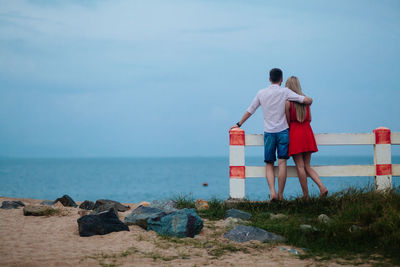 Rear view of couple standing at beach against sky