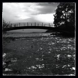 Bridge over river against cloudy sky