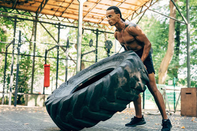 Full length of man lifting up tire on footpath