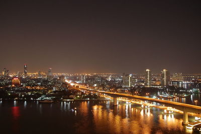 Illuminated buildings by river against sky at night