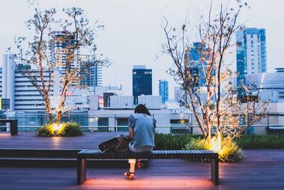 Rear view full length of woman on seat in city at dusk