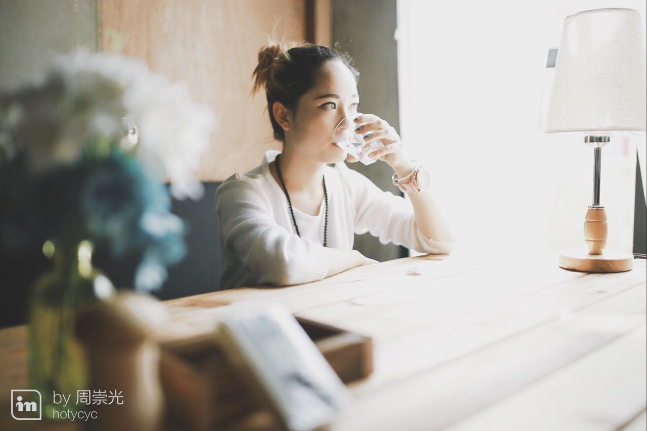 indoors, person, lifestyles, sitting, leisure activity, home interior, casual clothing, technology, young adult, wireless technology, three quarter length, waist up, holding, front view, table, communication, selective focus, book