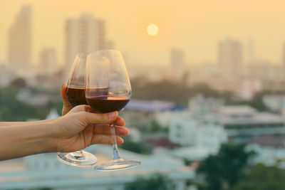 Cropped hand holding red wineglass at sunset 