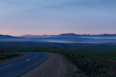 Road amidst field against sky during sunset